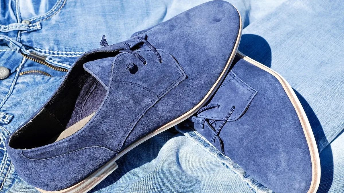 A pair of blue suede shoes with laces on a pair of light blue jeans.