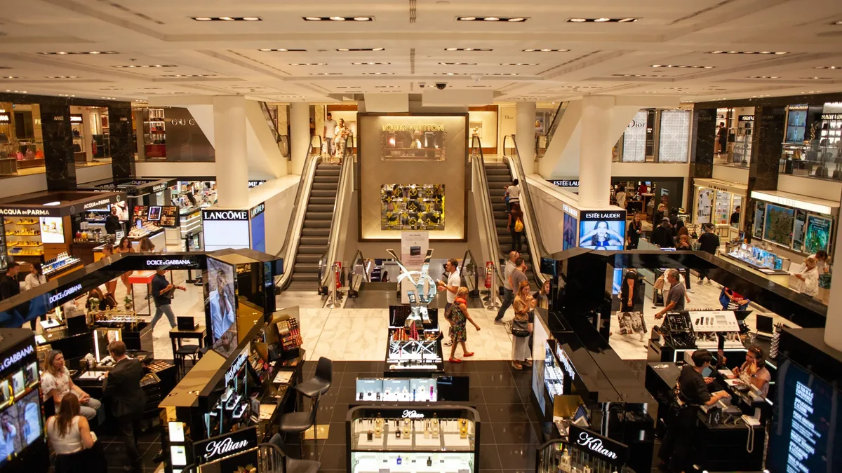 A large, multi-level department store with escalators, people, and various displays.