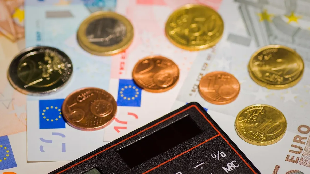 A collection of coins and banknotes from the European Union, with a calculator in the foreground.