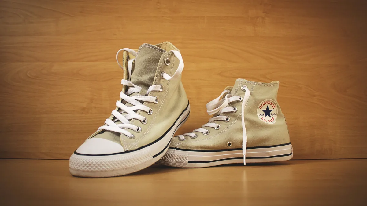 A pair of high-top Converse All Star sneakers, with one shoe propped up against the other, resting on a wooden surface.
